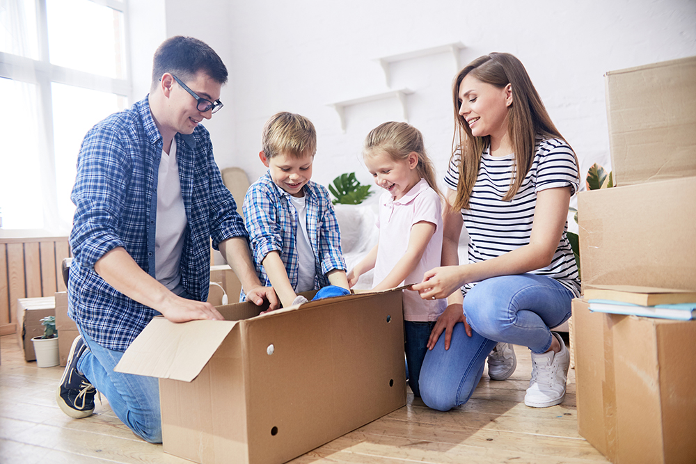 Unpacking Moving Boxes Enthusiastically Cheerful young family gathered together at spacious living room of new apartment and enthusiastically unpacking moving boxes with their stuff